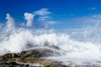 Waves splashing on rocks against sky