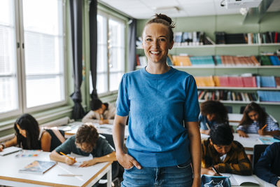 Portrait of happy female professor with hand in pocket standing in classroom at elementary school