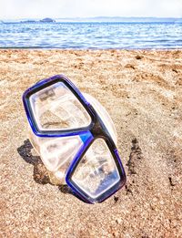 Sunglasses on sand at beach against sky