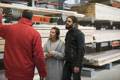 Rear view of salesman explaining wooden planks to couple in hardware store