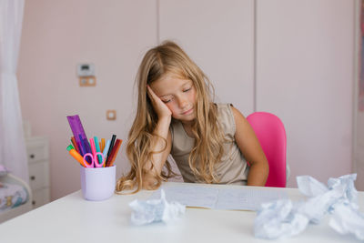 Cute caucasian girl of seven years old at her desk at home or at school is tired of doing homework