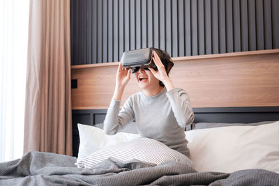 Young woman using virtual reality simulator sitting on bed at home