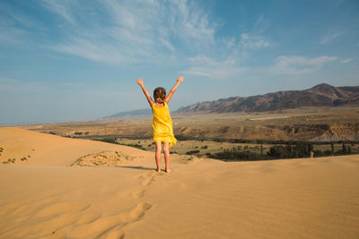 Rear view of woman standing on sand at desert against sky