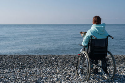 Caucasian woman in a wheelchair cuddling with a dog near the sea. 