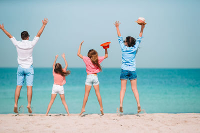Rear view of friends enjoying at beach against sky