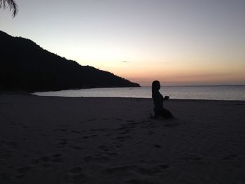 Silhouette man sitting on beach against clear sky