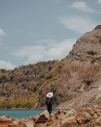 Rear view of man standing on rock against sky