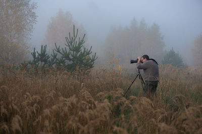 Man photographing while standing on field during foggy weather