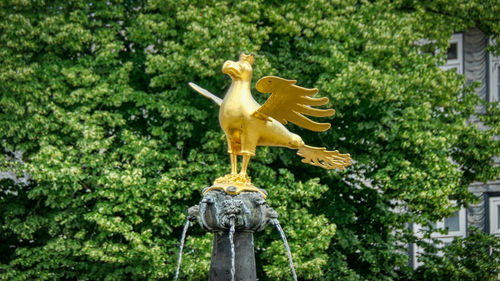 Statue of bird on plant against trees