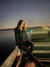 Woman sitting on railing against sky at night