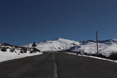 Road amidst snowcapped mountains against clear blue sky