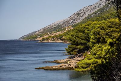 Scenic view of sea by mountain against clear sky