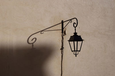Low angle view of street light hanging on wall and its shadow