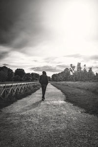 Rear view of man walking on field against sky