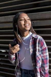 Young woman holding phone and singing while leaning against metallic built structure
