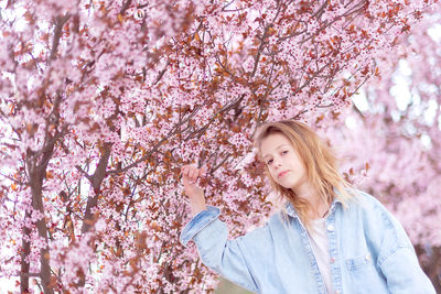 Portrait of young woman standing by cherry blossom tree