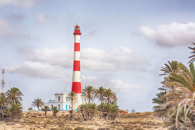 Lighthouse amidst trees and buildings against sky