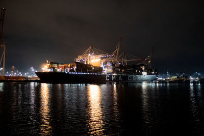 Illuminated harbor by sea against sky at night