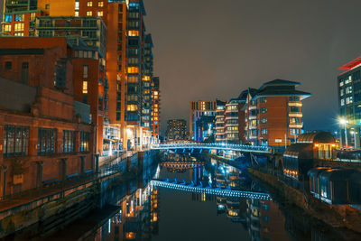 Illuminated bridge over canal amidst buildings in city at night