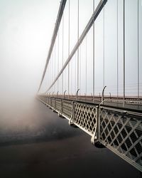Suspension bridge leading towards sky during foggy weather