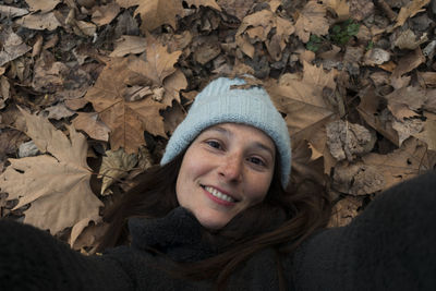 High angle portrait of smiling woman lying on autumn leaves