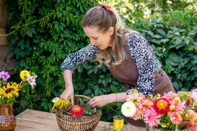 Cute florist girl collects a bouquet in a basket of autumn flowers