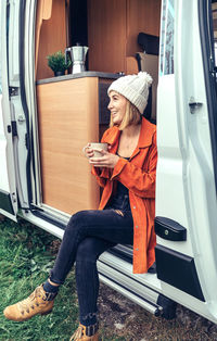 Woman drinking coffee sitting at the door of a camper van