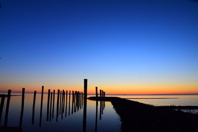 Silhouette wooden posts in sea against clear sky during sunset