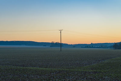 Electricity pylon on field against clear sky at sunset