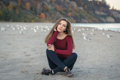 Portrait of smiling young woman sitting on sand at beach