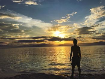 Rear view of silhouette man standing at beach during sunset