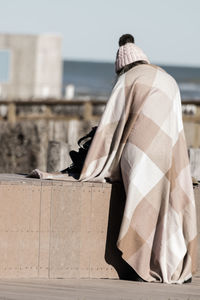 Rear view of man wearing blanket sitting outdoors