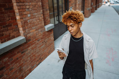 Young positive multiracial man in stylish clothes holding smart mobile phone while walking