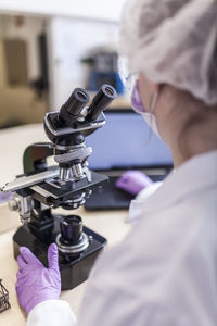 Back view of anonymous woman scientist looking through microscope at laboratory