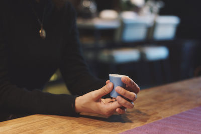 Midsection of woman holding coffee cup sitting at cafe