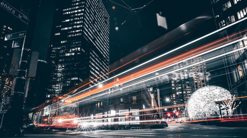 Trolley on road by illuminated buildings in city at night long exposure 