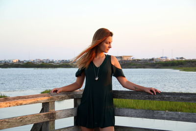 Thoughtful woman standing on pier over sea against sky