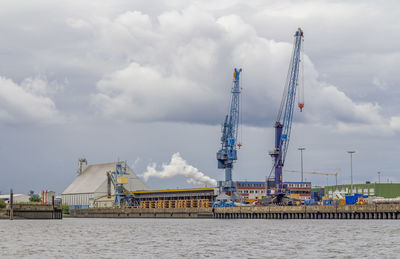 Cranes at commercial dock against sky