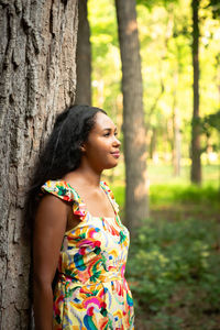 Beautiful mixed race african american woman wearing a yellow floral dress leaning against a tree