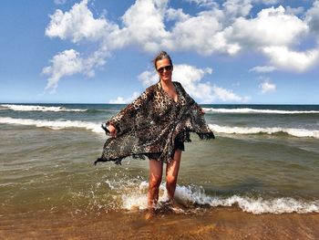 Portrait of smiling woman standing at beach against sky 