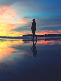 Rear view of silhouette woman walking at beach against sky during sunset