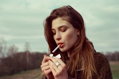 Beautiful young woman smoking cigarette standing outdoors
