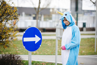 Smiling young woman in costume standing by directional sign on field