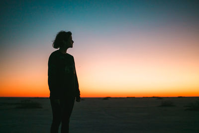 Silhouette man standing on beach against clear sky during sunset