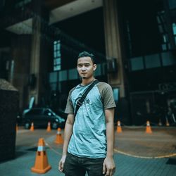 Young man looking away while standing on street in city