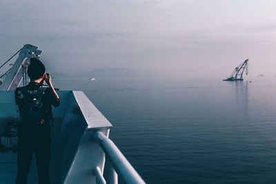 Rear view of photographer photographing sea while sailing in boat