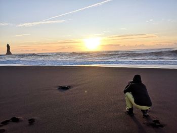 Rear view of men on beach against sky during sunset