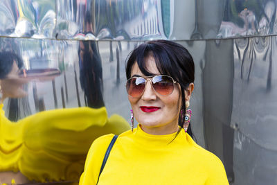 Fashionable mature woman wearing yellow top and sunglasses in city