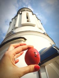 Low angle view of person holding apple against sky