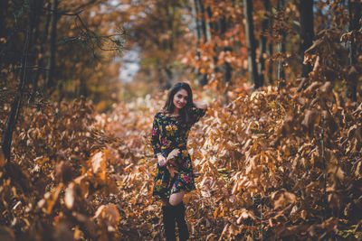 Portrait of young woman standing by tree in forest during autumn